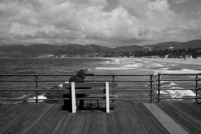 Bench on pier by sea against sky