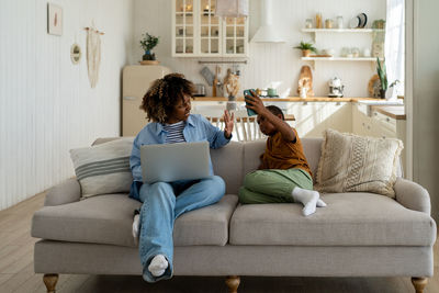 Young woman using phone while sitting on sofa at home