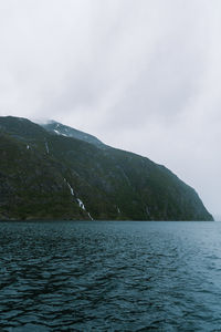 Scenic view of sea by mountain against sky