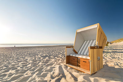 Hooded beach chair on shore against clear sky