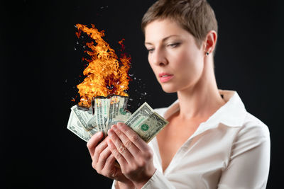 Portrait of young woman holding paper currency against black background