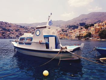 Sailboats moored on sea by buildings against sky