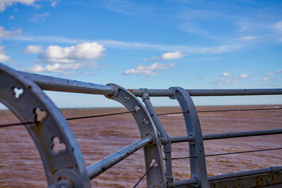 Close-up of metal railing by sea against sky