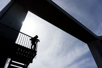 Low angle view of silhouette man standing on bridge against sky