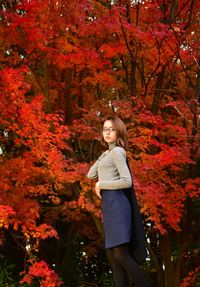 Portrait of young woman standing by trees during autumn