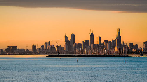 City at waterfront against sky during sunset