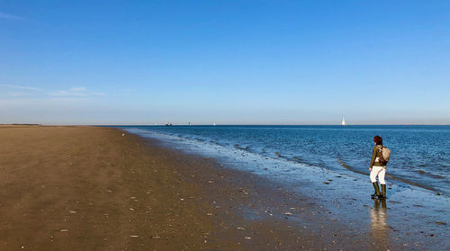 Rear view of man standing on beach against sky