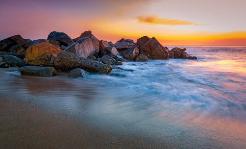 Rocks in sea against sky during sunset