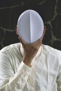 A fine art portrait of a man in indonesian islamic shirt hide his face with the religious white cap.