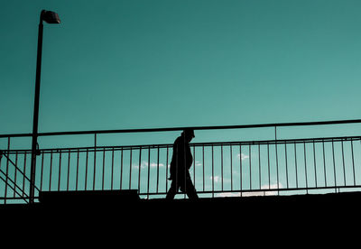 Silhouette woman walking on railing against clear sky