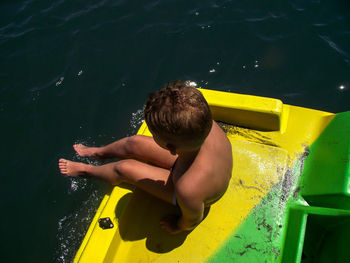 High angle view of shirtless boy sitting on boat over water