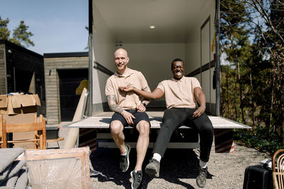 Portrait of smiling multiracial movers sitting in trunk of delivery truck