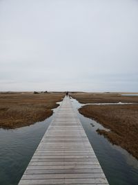 Boardwalk leading towards pier against sky