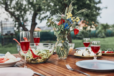 Dinner in an apple orchard garden on wooden table with salads and wine decorated with flowers