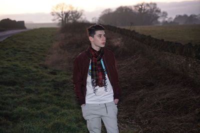 Young man looking away while standing on grassy field