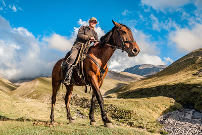 A cowgirl shepherd rider on a horse standing on a mountain valley on autumn day sky with clouds