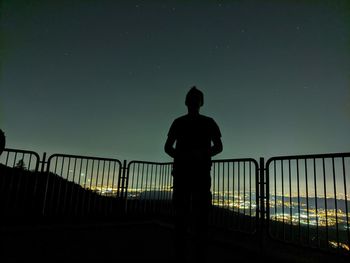 Rear view of silhouette man standing on bridge against sky at night