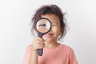 Portrait of girl looking through magnifying glass against white background