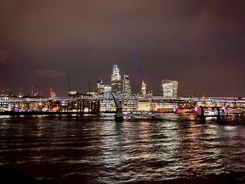 Illuminated city by river against sky at night