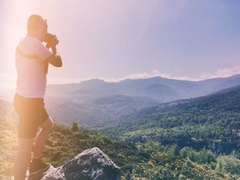 Man photographing mountains against sky on sunny day