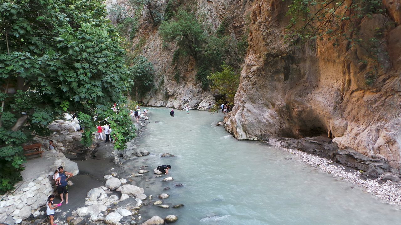 water, tree, rock - object, tourism, travel, large group of people, vacations, non-urban scene, tourist, tranquility, nature, tranquil scene, river, travel destinations, person, scenics, rock formation, beauty in nature, weekend activities, cliff, flowing, mountain, stream, riverbank, day, rocky mountains, outdoors, remote, swimming