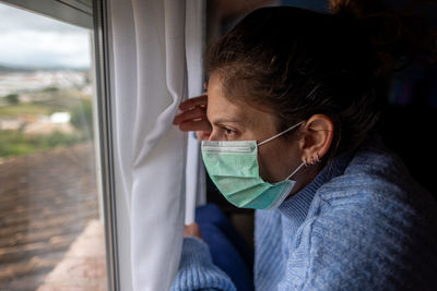 Close-up of woman wearing mask looking through window at home