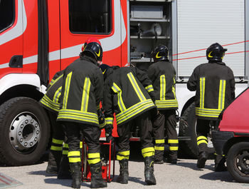 Rear view of firefighters working by firetruck on road