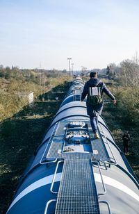 Full length rear view of man walking on top of train against sky