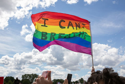 Low angle view of hand holding flag against sky
