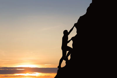 Silhouette man on rock against sky during sunset