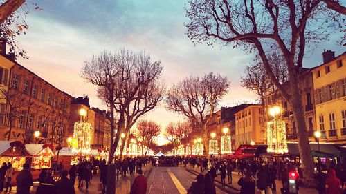 People on illuminated street against sky at dusk