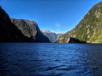 Scenic view of sea by mountains against clear blue sky