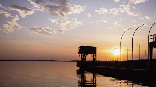 Scenic view of street poles and crane and their reflections on the sea under the sky during sunset