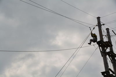Low angle view of worker on telephone pole against cloudy sky