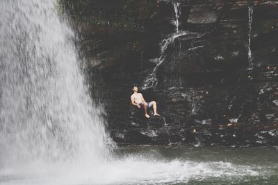 Man sitting on rock by waterfall