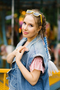 Sensual caucasian woman with blue pigtails and bright makeup in a denim vest in an amusement park