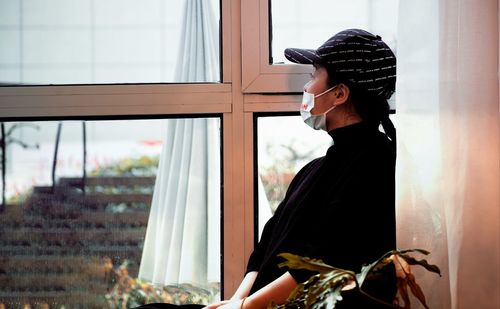 Side view of young woman looking through window