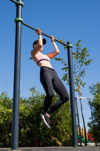 . happy woman in sportclothes working out on the sports ground in sunny summer day, doing pull ups