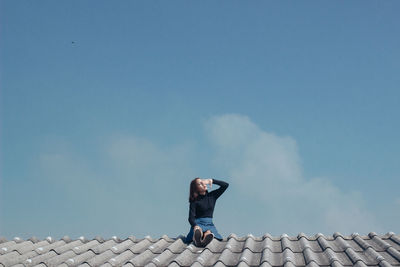 Low angle view of woman on roof against sky