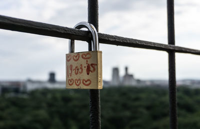 Close-up of date and heart shape on padlock locked to metallic fence against sky