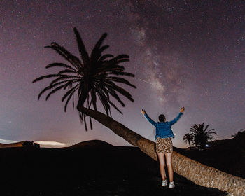 Rear view of woman with arms outstretched standing against sky at night