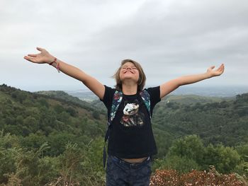 Young woman with arms outstretched standing on mountain against sky