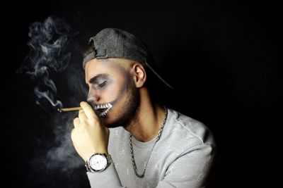 Portrait of man smoking cigarette against black background