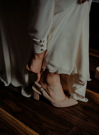 Low section of bride wearing heels on wooden floor