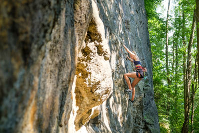 Low angle view of woman rock climbing on wall outdoors