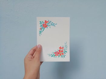 Cropped hand of person holding blank greeting card against wall