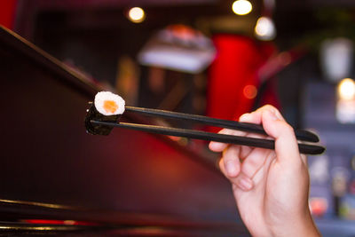 Cropped image of person holding sushi from chopsticks