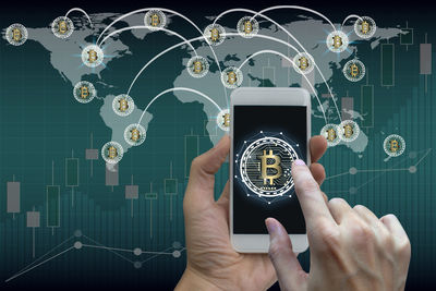 Close-up of hand using mobile phone with bitcoin symbol against world map