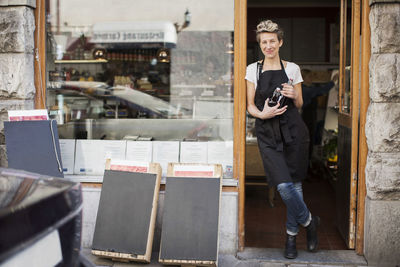 Portrait of smiling saleswoman standing at supermarket entrance