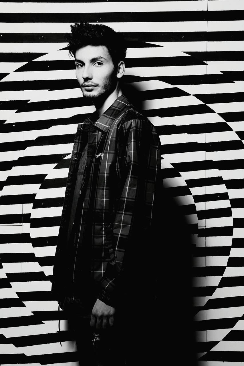 one person, standing, young adult, real people, young men, waist up, casual clothing, lifestyles, leisure activity, portrait, looking at camera, front view, pattern, striped, three quarter length, wall - building feature, indoors, confidence, hairstyle